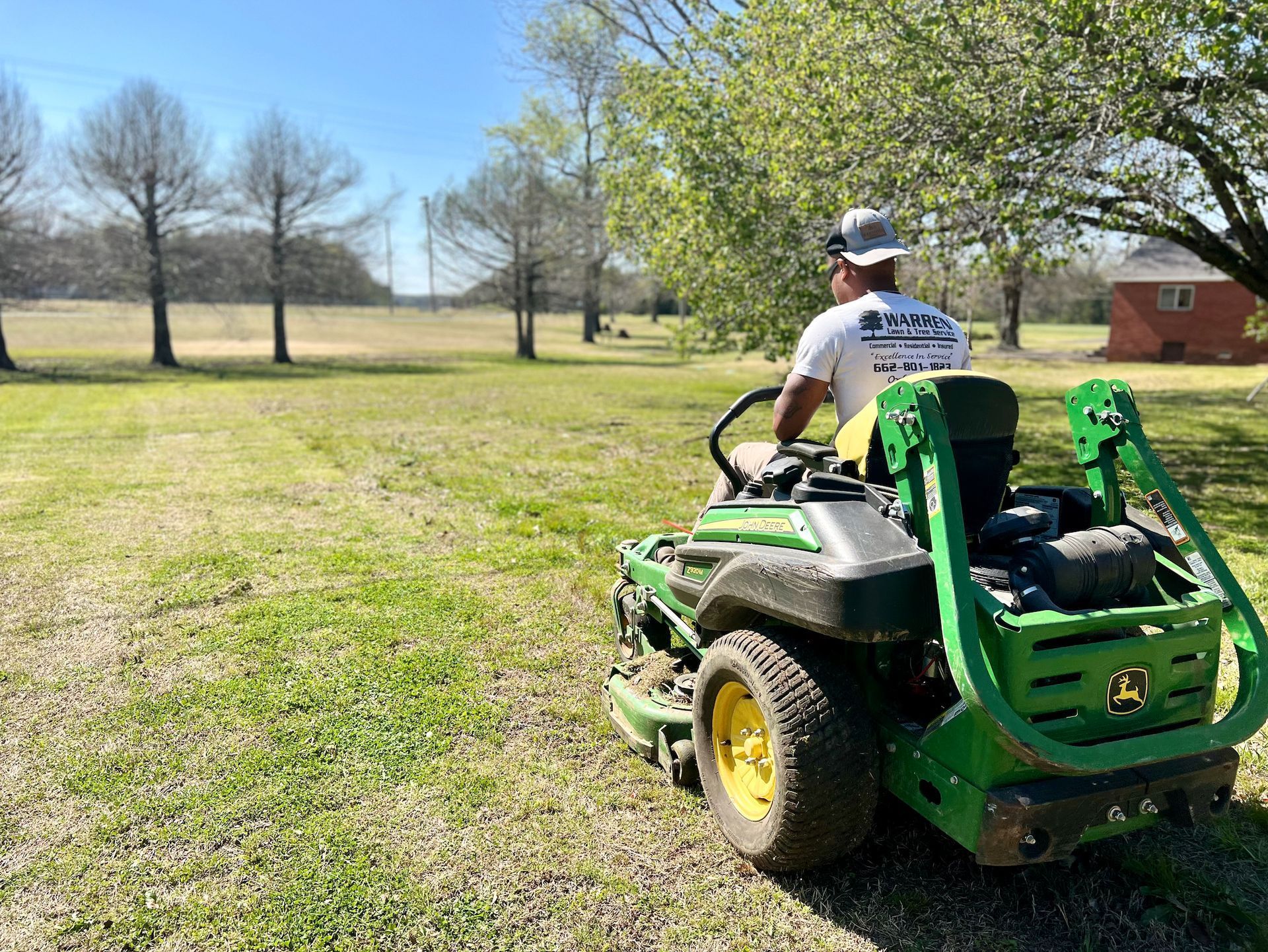 A person on a green John Deere mower cuts grass in a yard on a sunny day.