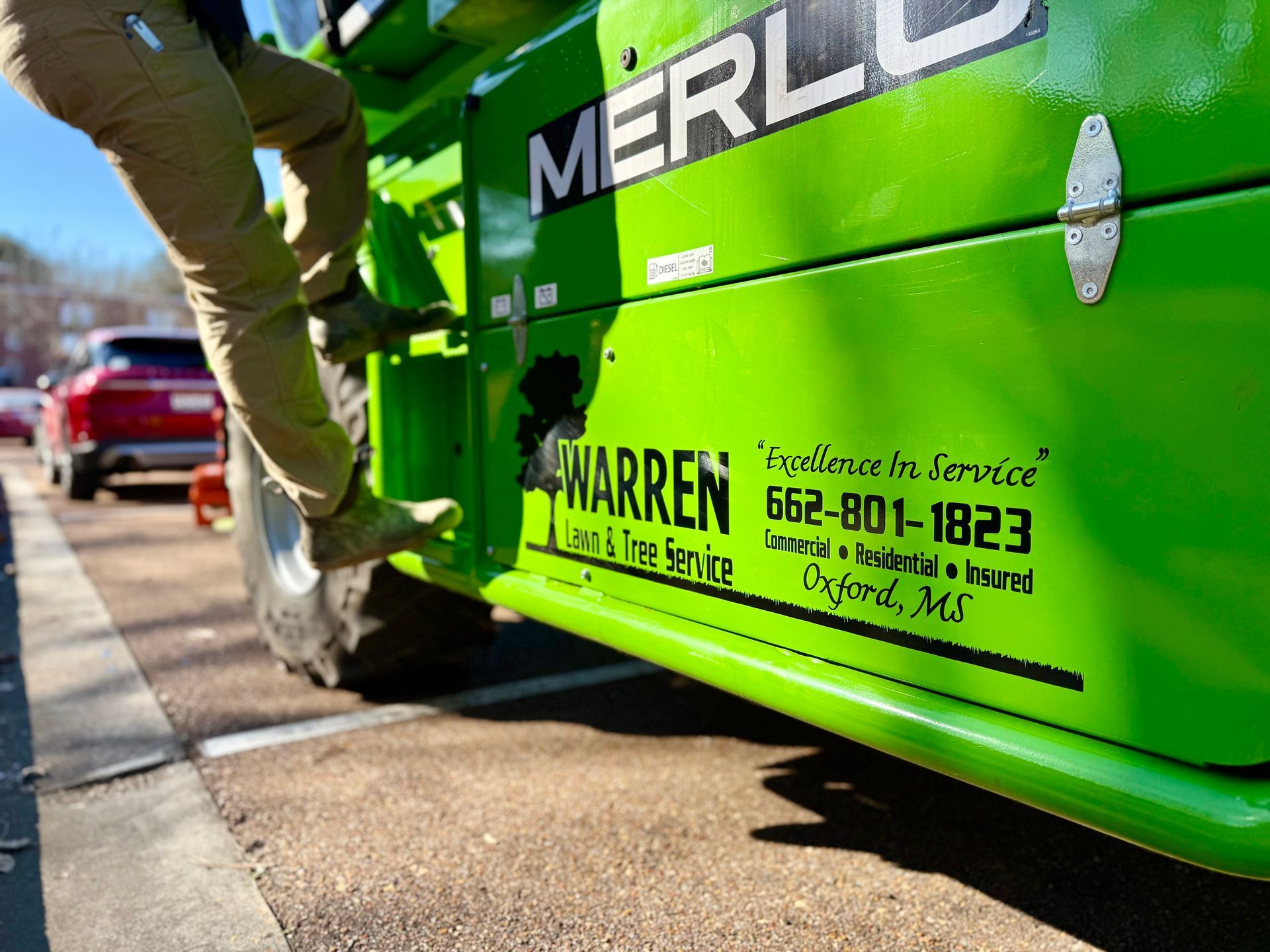 Person climbing onto a bright green Merlo machine. The machine has