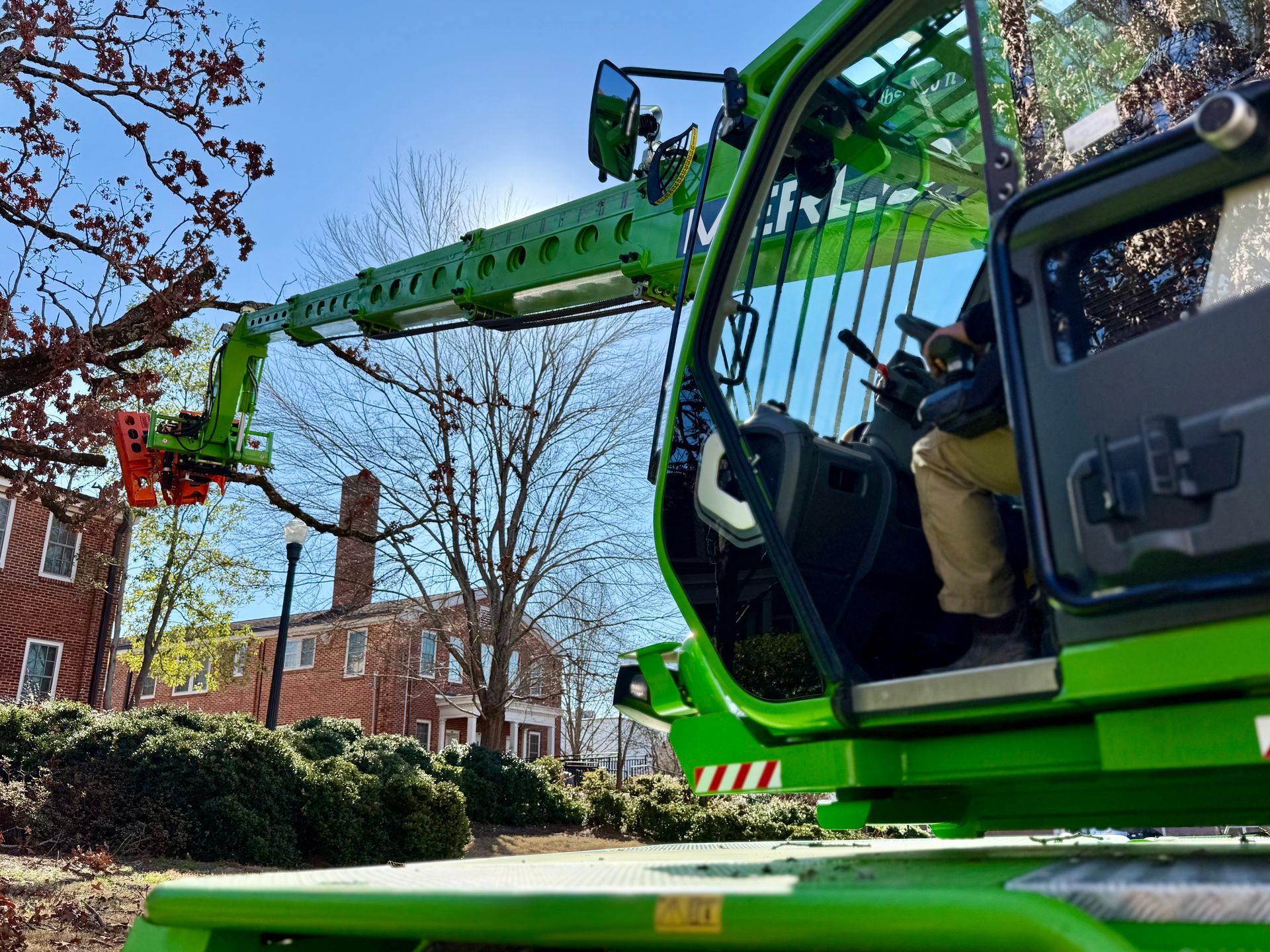 Green tree trimming machine with a person operating it, trimming branches.