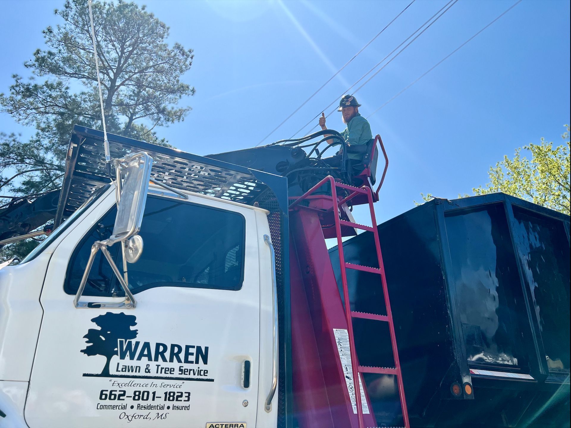 Man in lift platform trimming tree branches from a truck labeled Warren Lawn & Tree Service.