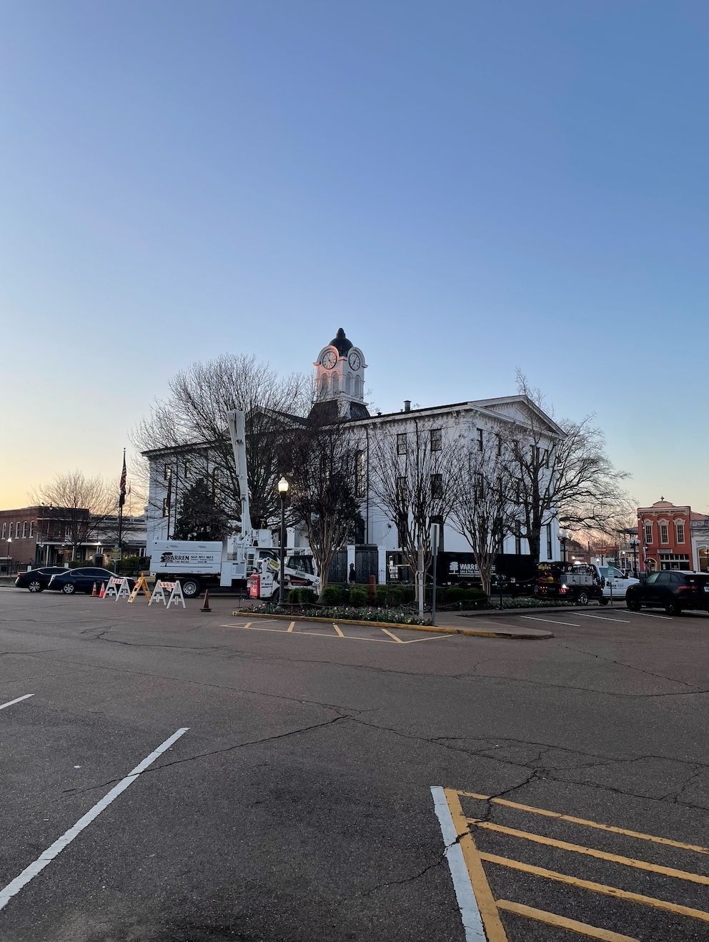 White courthouse with a clock tower under a clear sky; parked cars in the street.