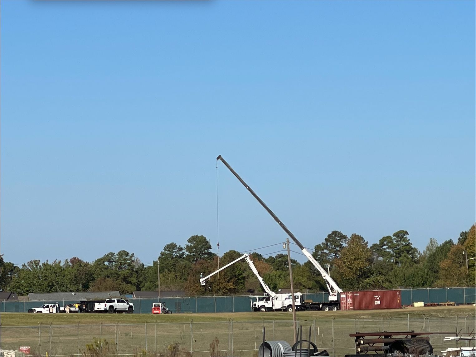 A large crane lifting something near a construction site. Blue sky and trees in the background.