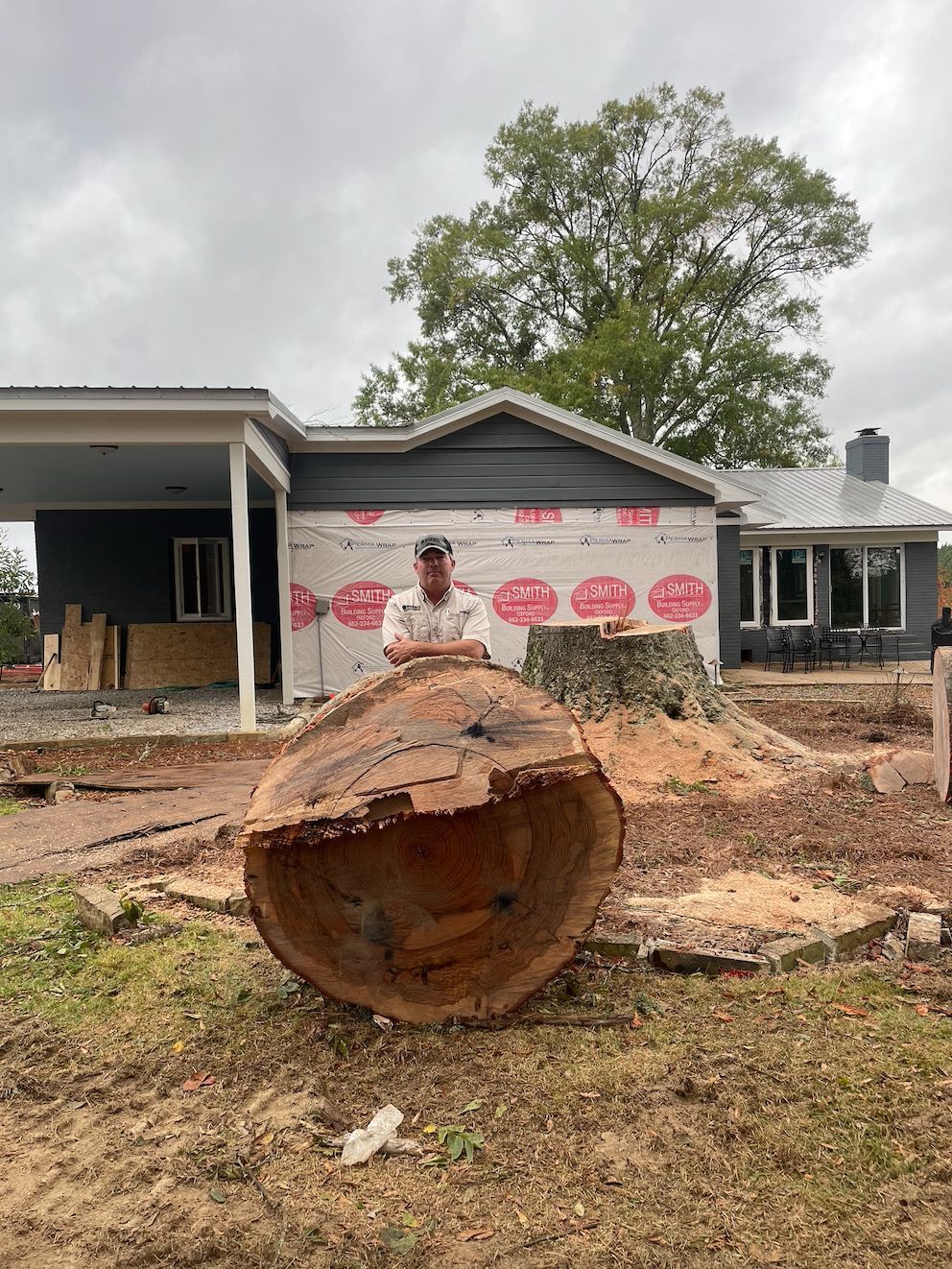 Man standing next to large tree trunk in front of a house under construction.