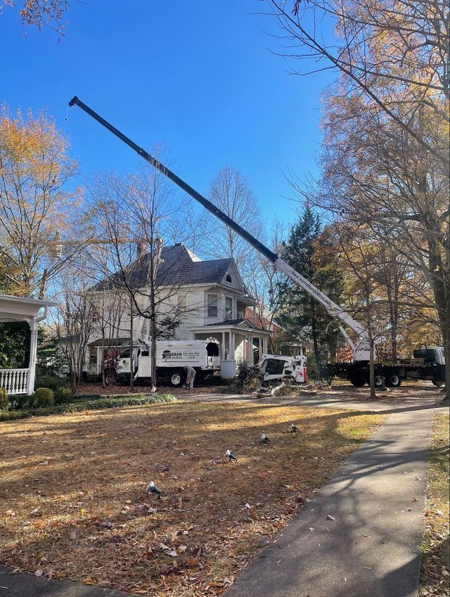 A crane lifting equipment near a two-story white house with fall foliage on a sunny day.