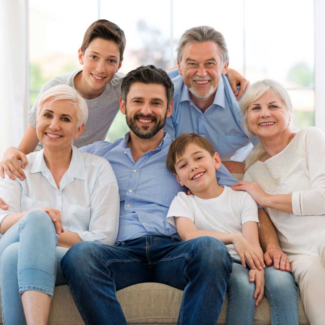 Family of seven smiling, sitting together on a couch indoors.