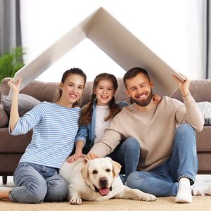Family of three, and a dog, smiling, under a roof-shaped cover in a living room.