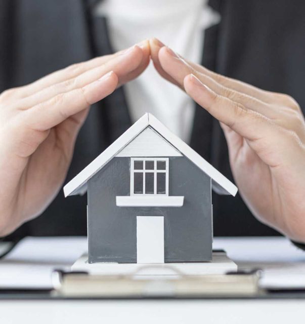 Hands cupped over a small house model, symbolizing protection and home security.