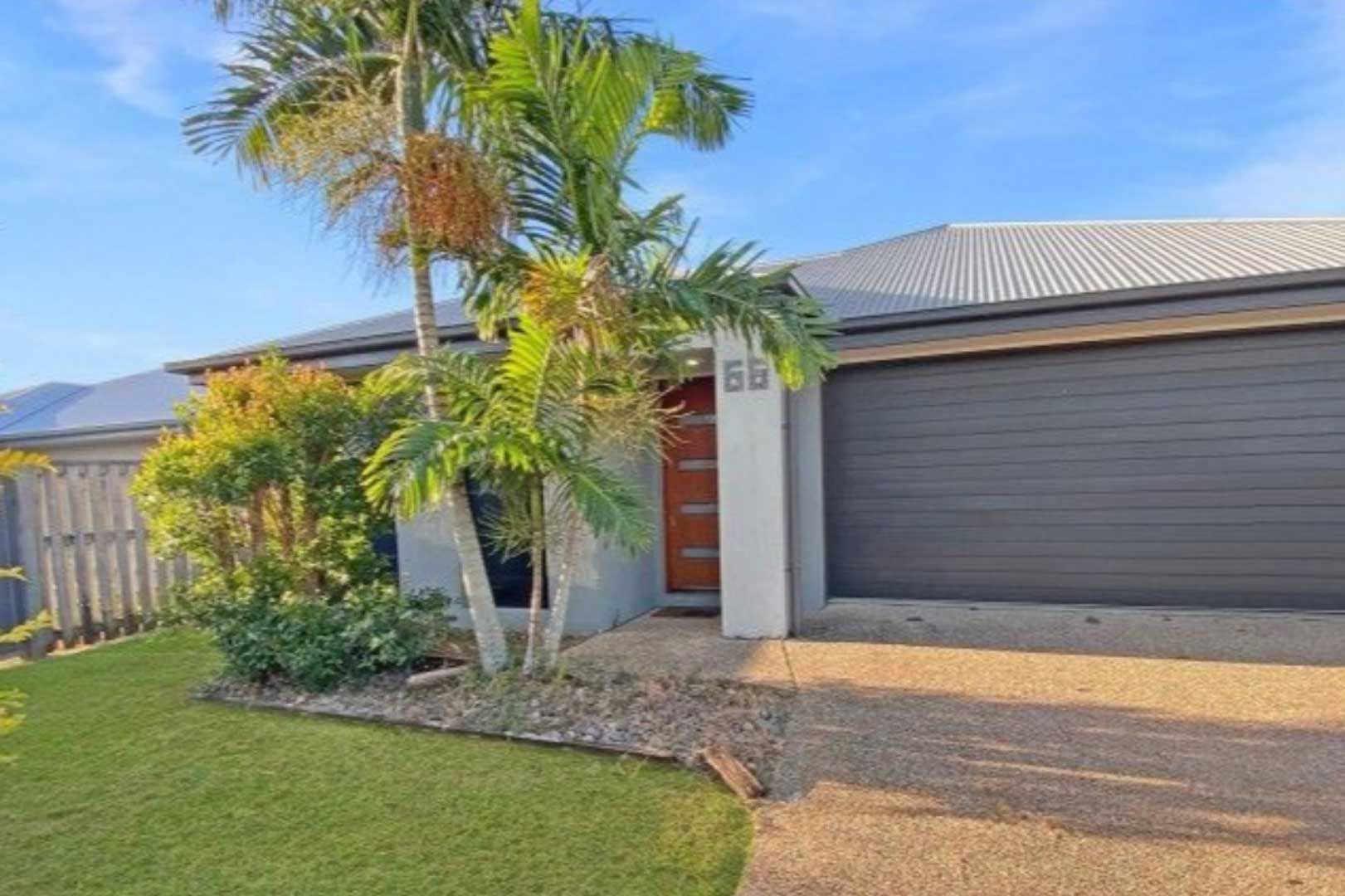 House exterior with grey garage door, front door, palm trees, and green lawn.
