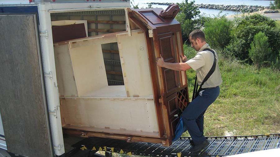 A man is carrying a piece of furniture out of a truck from Cupboard Wagon cabinet delivery services