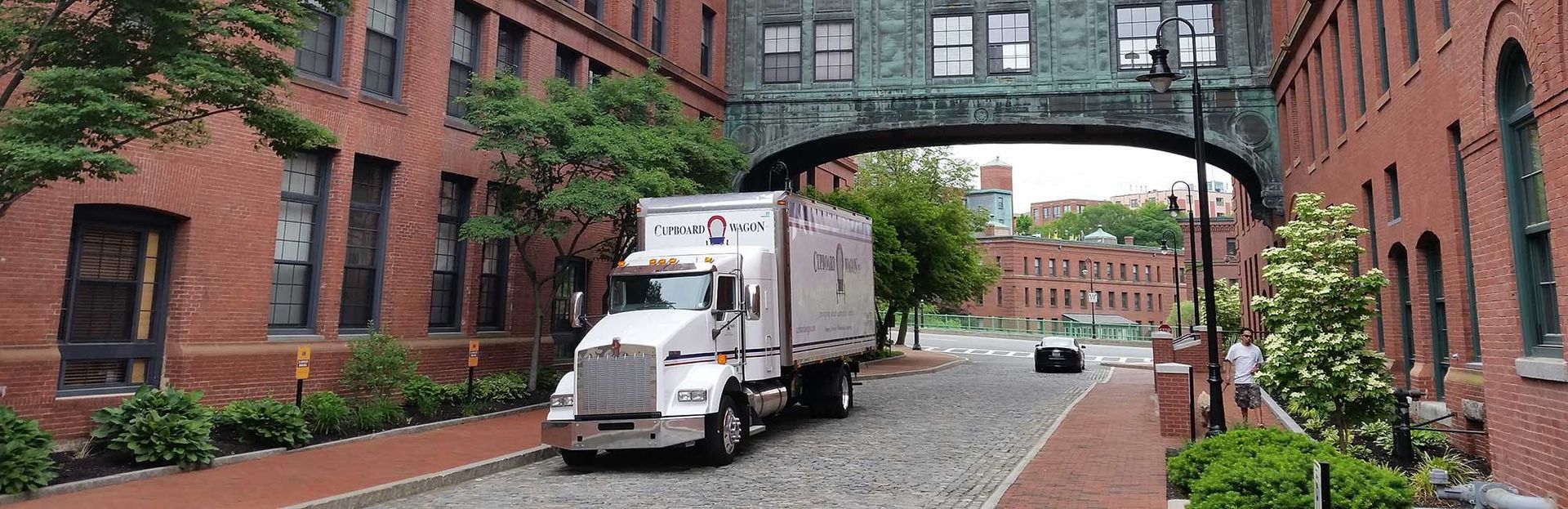 A white truck is driving down a cobblestone street under a bridge.