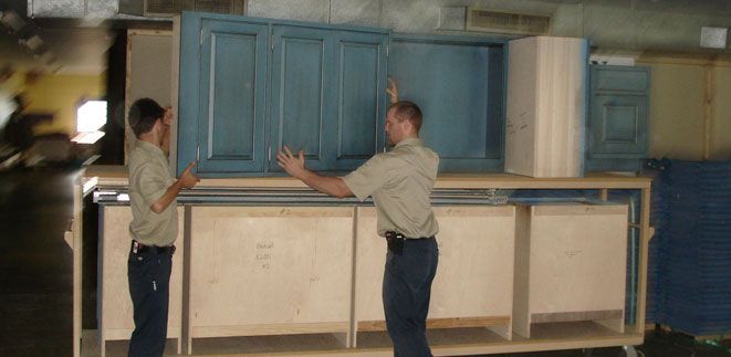 Two men are working on a blue cabinet in a warehouse from Cupboard Wagon cabinet delivery services