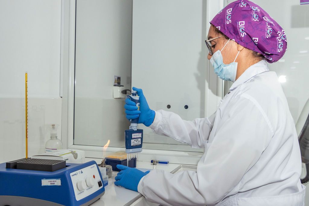 Un técnico de laboratorio, vestido con bata blanca y gorro morado, maneja un instrumento de laboratorio azu