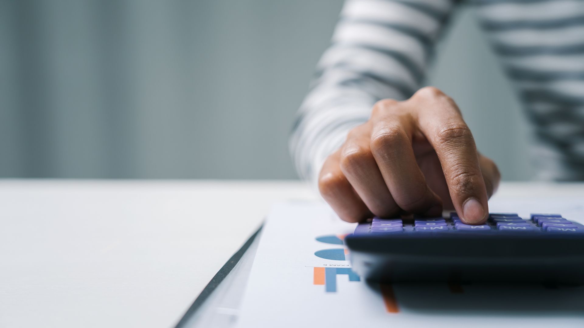 A person's hand using a calculator on a white surface with financial documents.