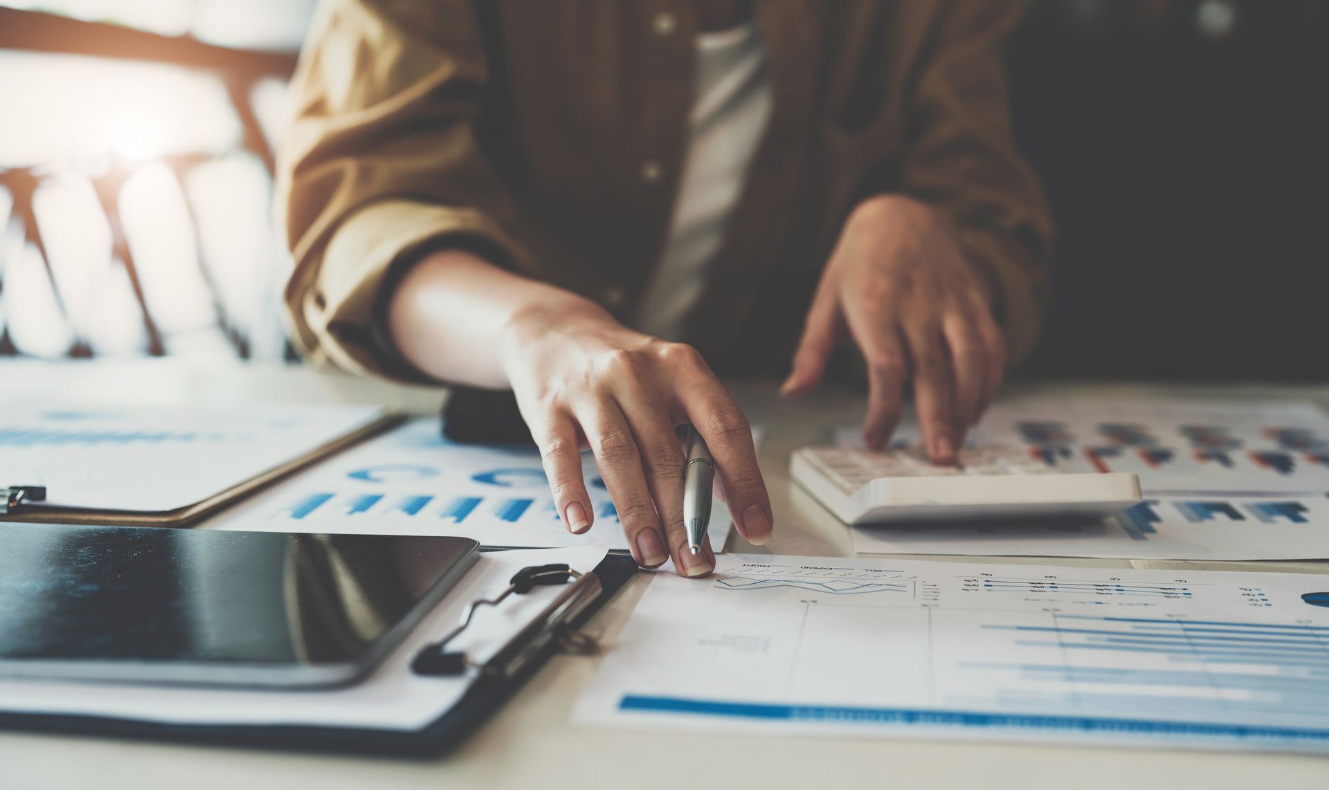 Person using a calculator and reviewing financial documents with graphs. Person using a calculator and reviewing financial documents with graphs.