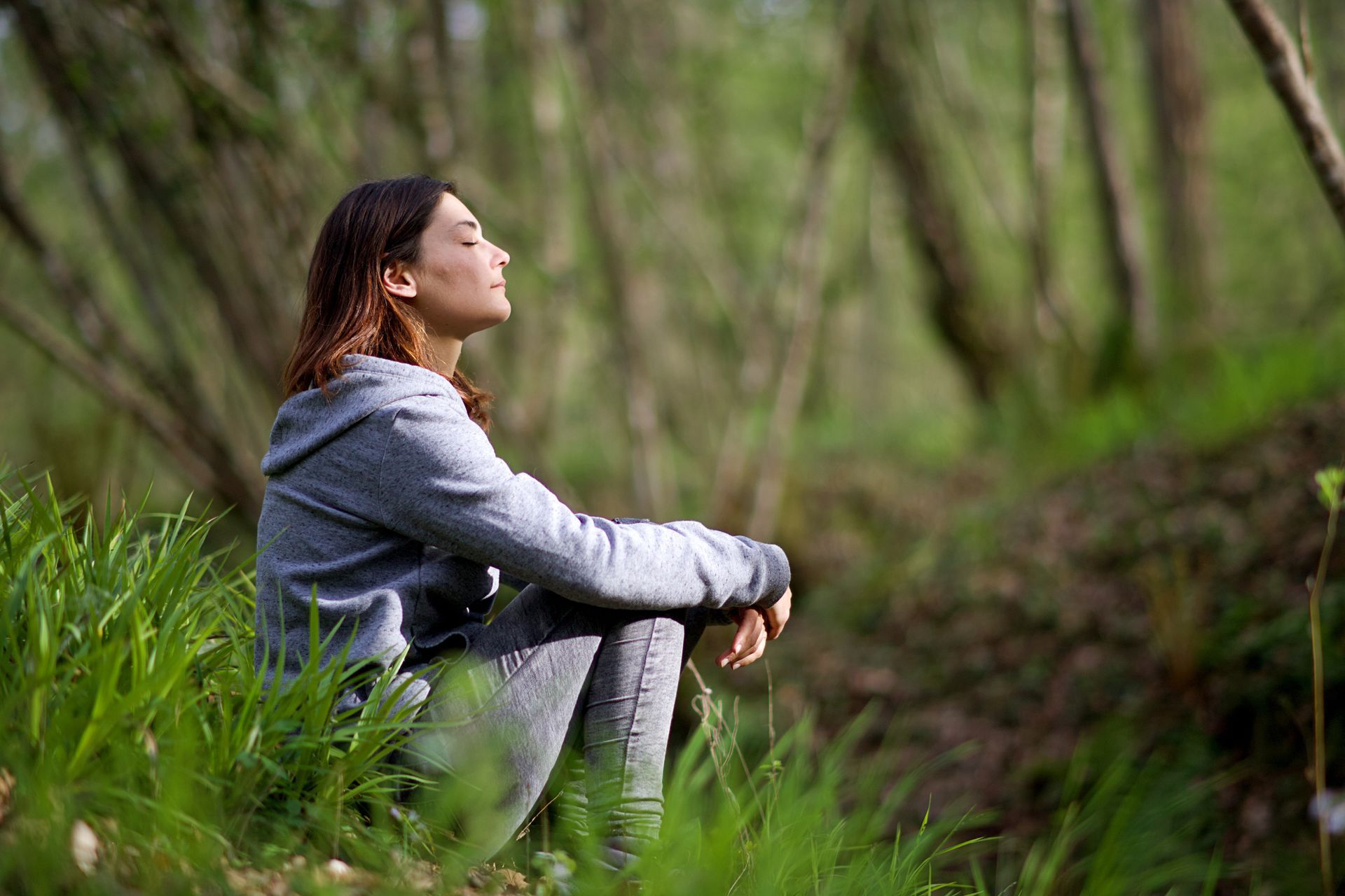 Person sitting in a forest, gazing upward in a gray jacket and leggings. Person sitting in a forest, gazing upward in a gray jacket and leggings.