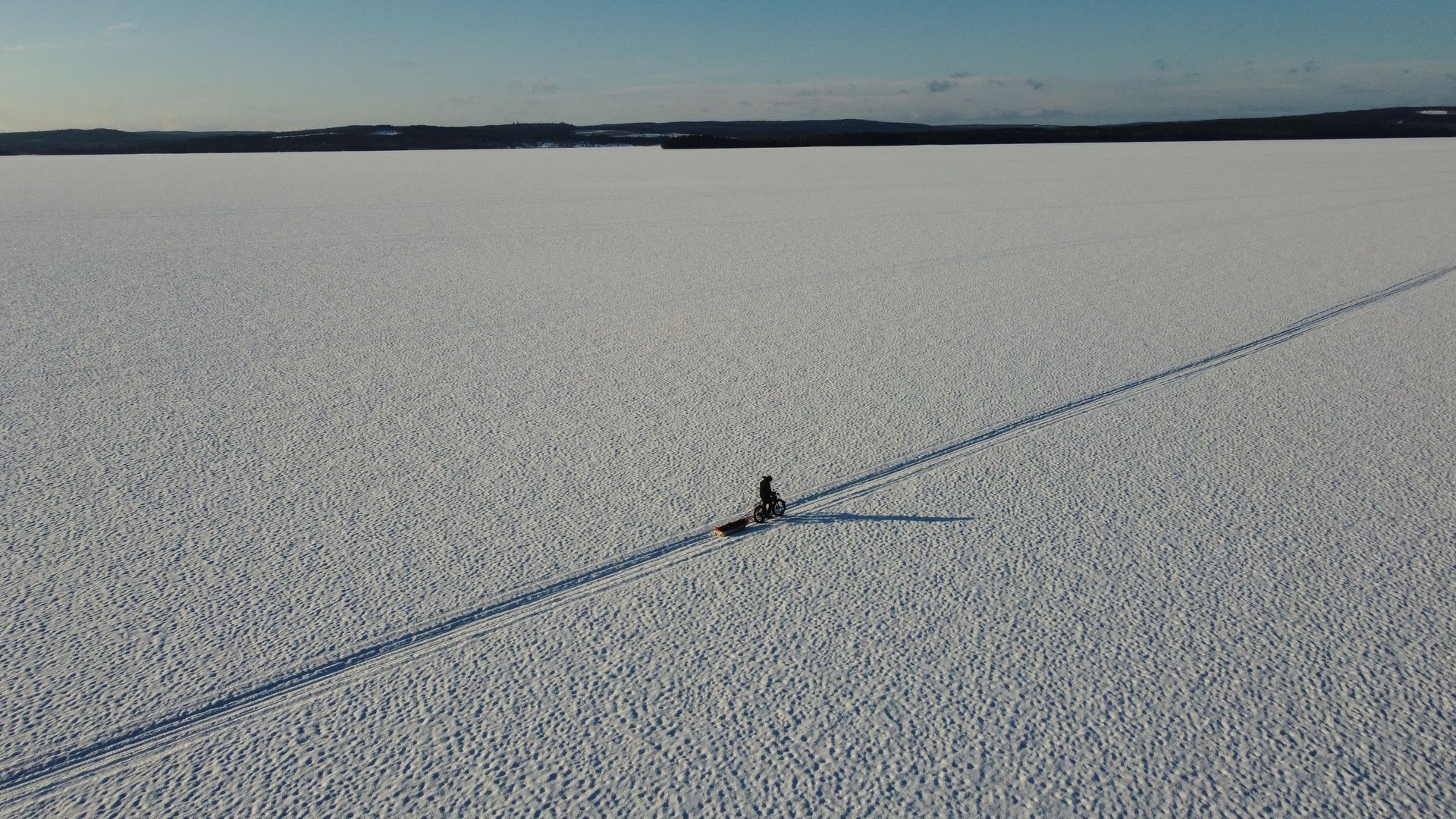 Person on a snowy frozen lake with a long shadow stretching across the ice