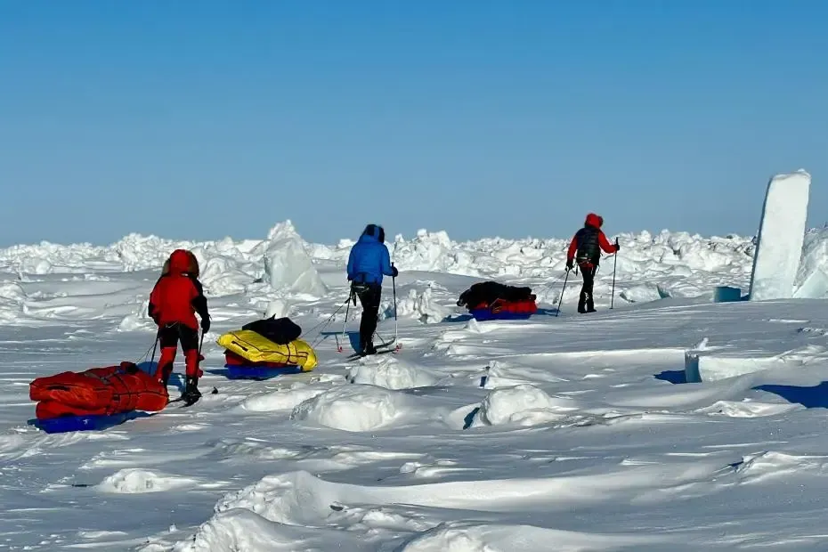 Hikers walking across a snowy glacier above a blue ice crevasse