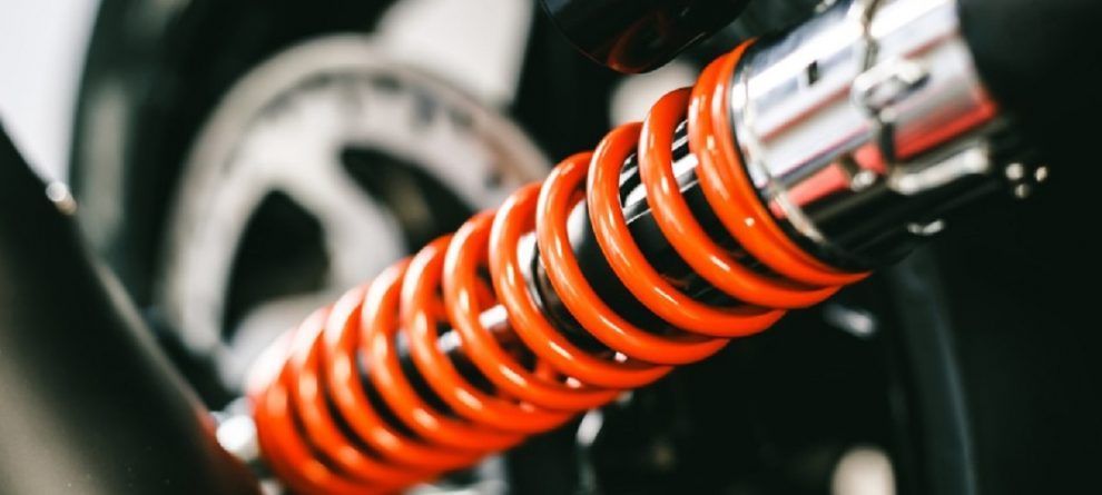 Primo piano di un ammortizzatore per motocicletta con molla arancione e cilindro cromato.