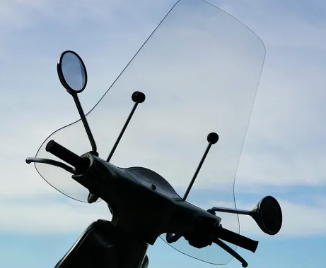 Sagoma del manubrio di uno scooter con specchietti e parabrezza contro un cielo blu.