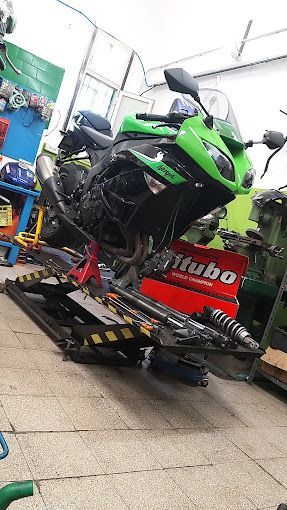 Motocicletta verde e nera su un ponte sollevatore in un'officina, sono visibili vari pezzi.