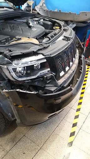 SUV nero con danni alla parte anteriore, paraurti mancante. Cofano aperto, fari visibili in officina.