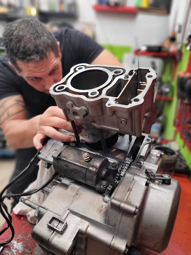 Uomo che assembla il motore di una motocicletta in un'officina, concentrandosi sul blocco cilindri.