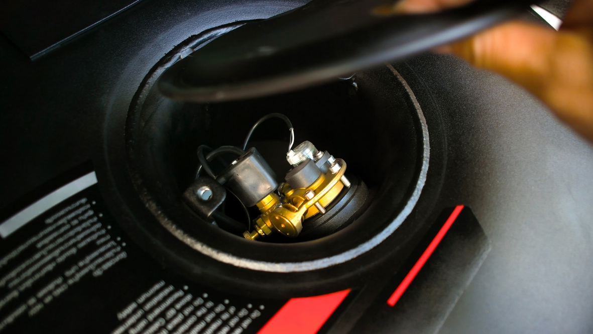 Serbatoio del carburante aperto con componenti interni visibili, probabilmente di un veicolo. Nero e oro.