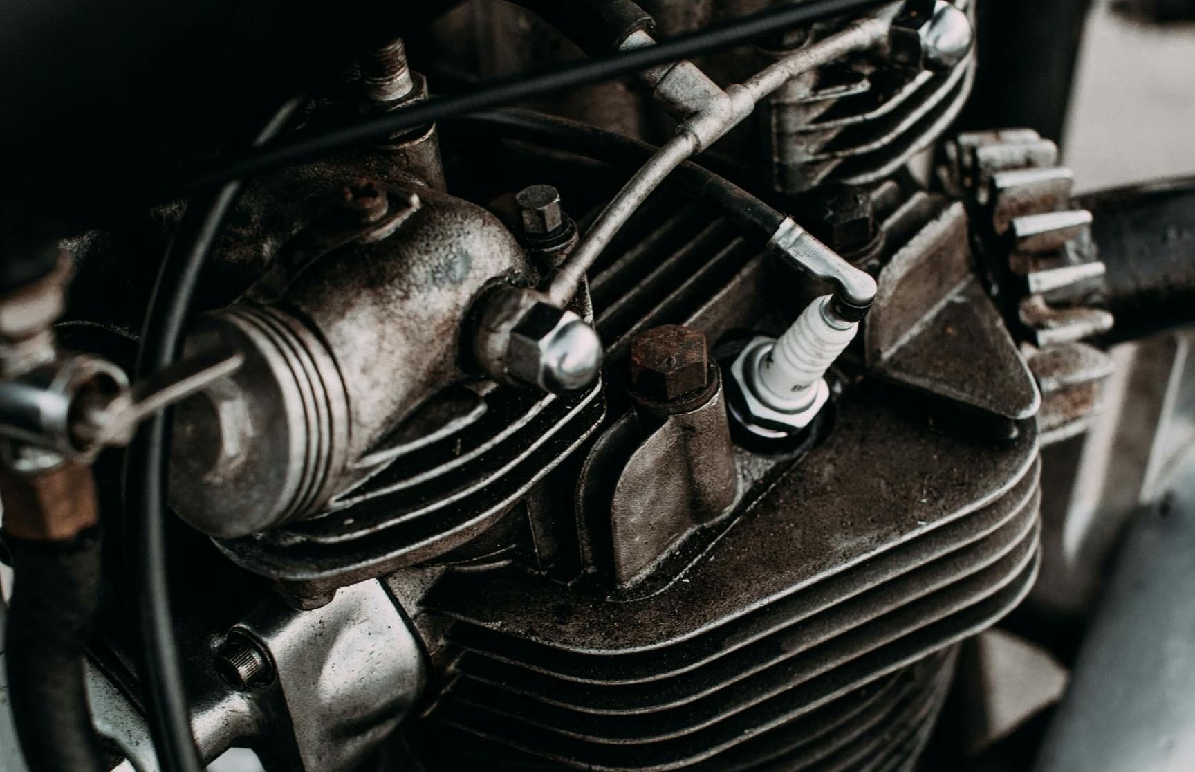 Primo piano del motore di una motocicletta d'epoca con candela e alette di raffreddamento a vista.