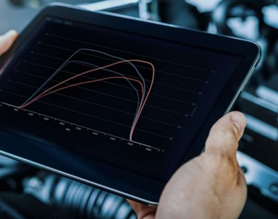 Mani che tengono un tablet su cui sono visualizzati i grafici delle prestazioni del motore nel vano di carico di un veicolo.