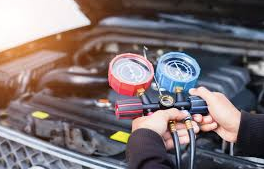 Un meccanico usa degli indicatori per controllare il sistema di aria condizionata di un'auto nel vano motore.