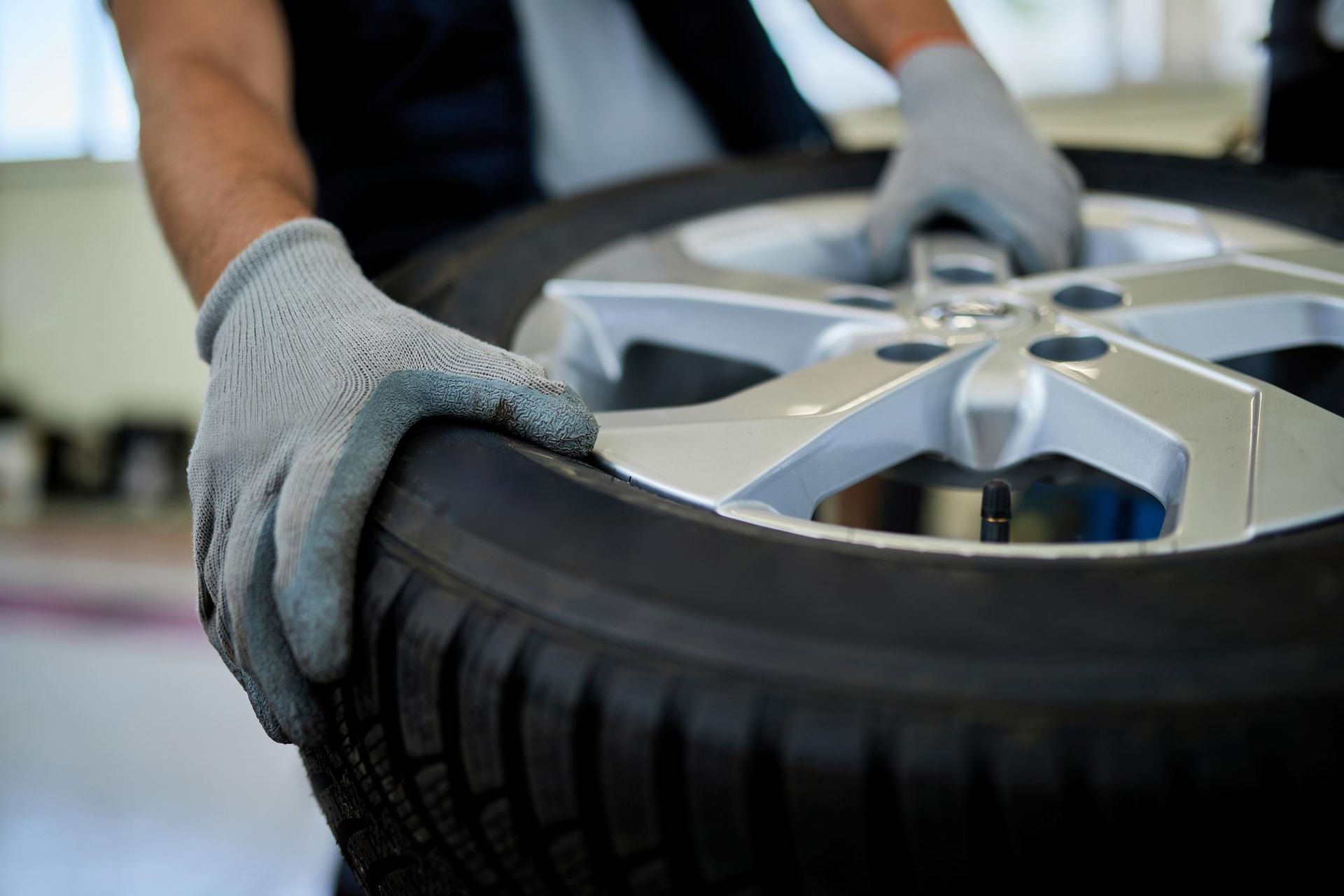 Persona che indossa guanti e trasporta uno pneumatico per auto con cerchione argentato.