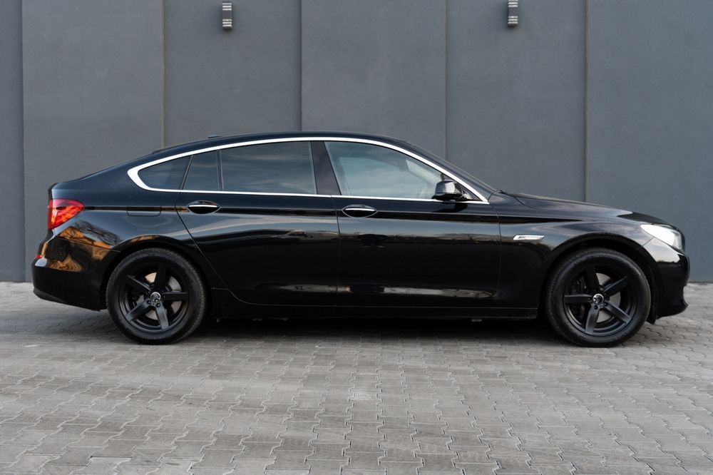 A black car is parked in front of a gray wall.