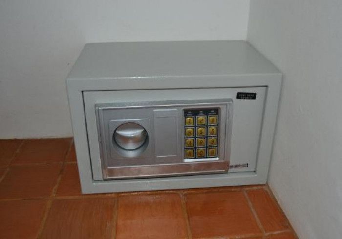 Um cofre cinza com teclado digital e botão redondo, instalado sobre piso de azulejo marrom.