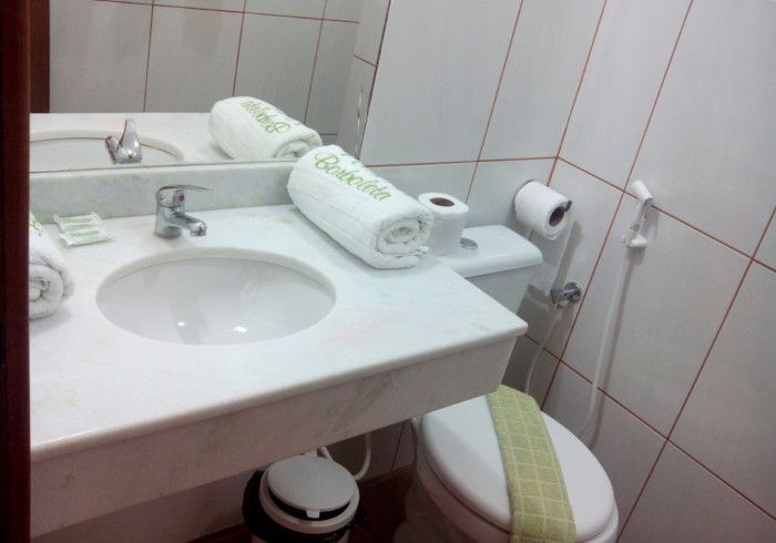 Banheiro com pia, vaso sanitário e toalhas enroladas sobre a bancada. Esquema de cores branco e verde claro.