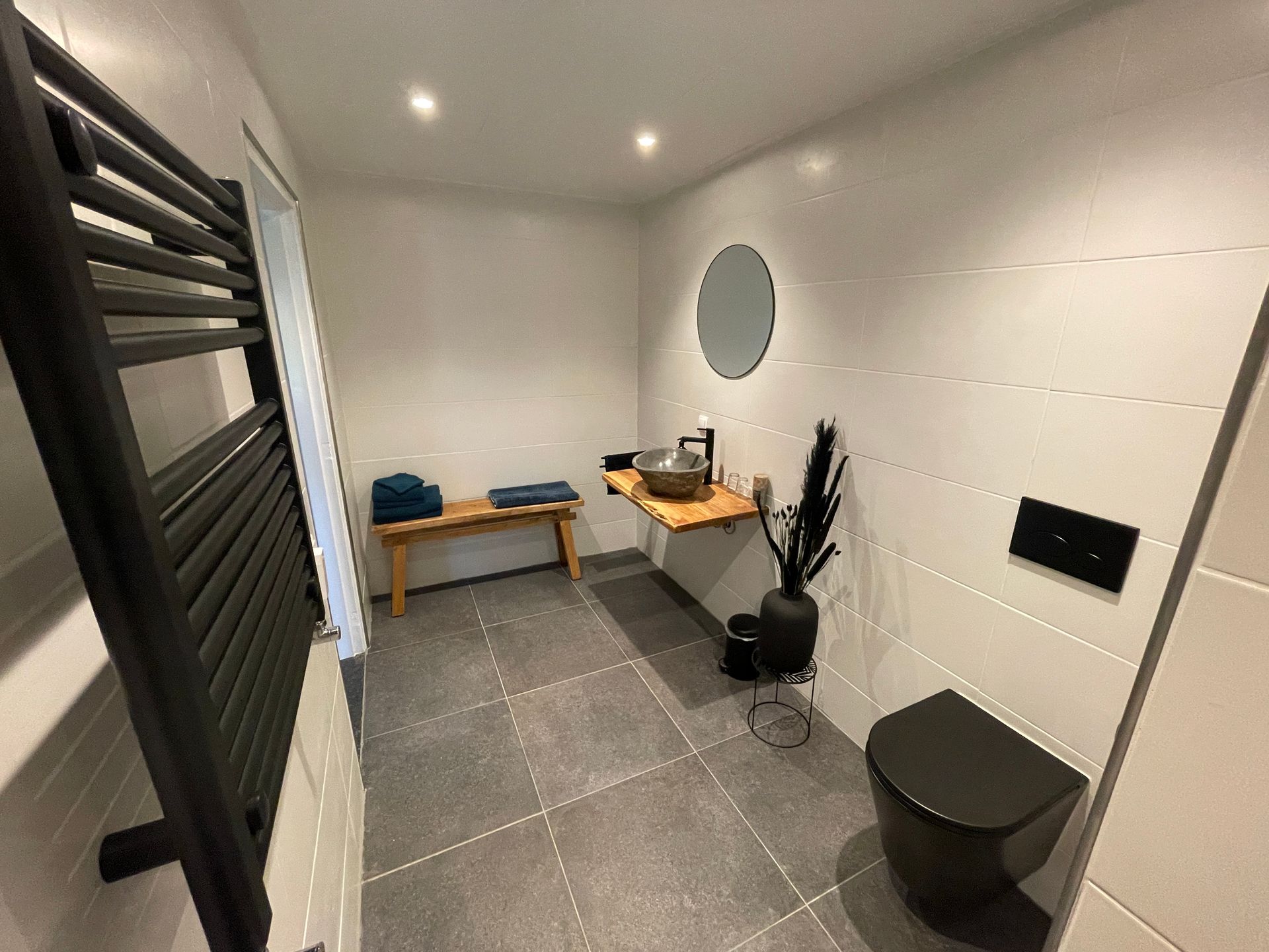 Moderne badkamer met zwart toilet, wastafel, handdoekrek en houten accenten.