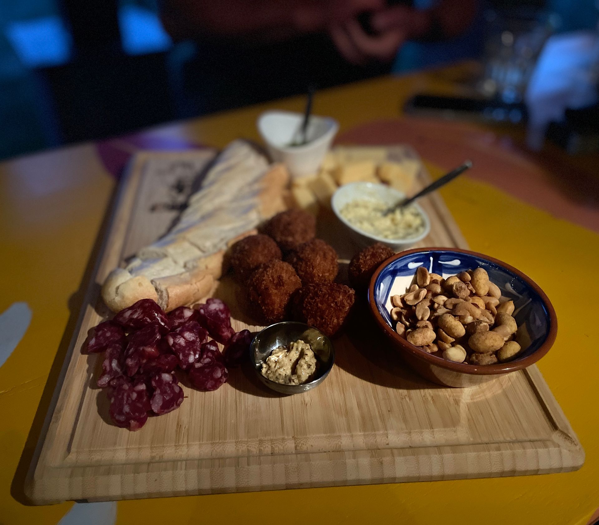 Charcuterieplank met stokbrood, salami, kaas, gefrituurde balletjes, pinda's en dipsauzen.