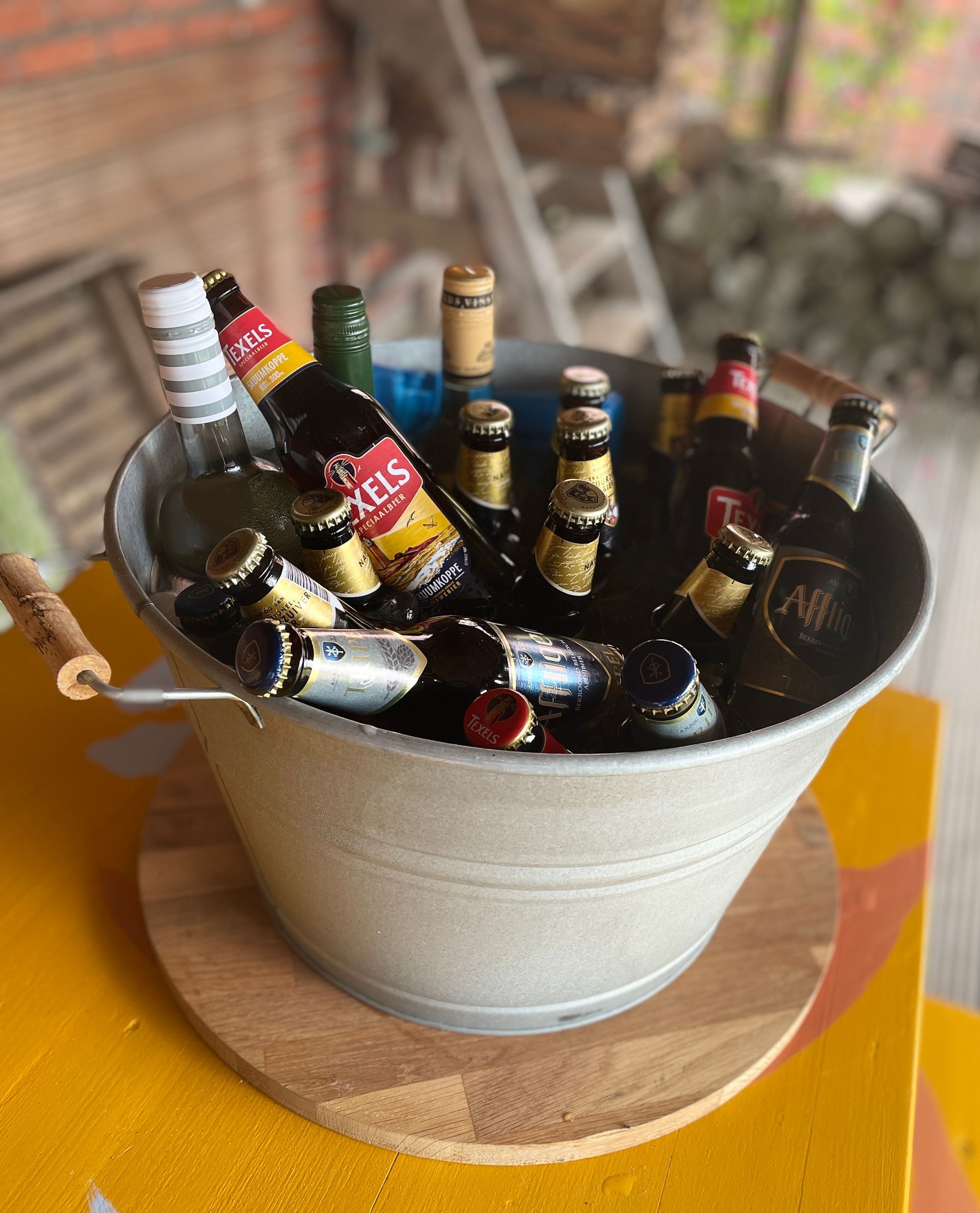 Een emmer met bierflesjes op een houten onderzetter, die op een gele tafel staat.