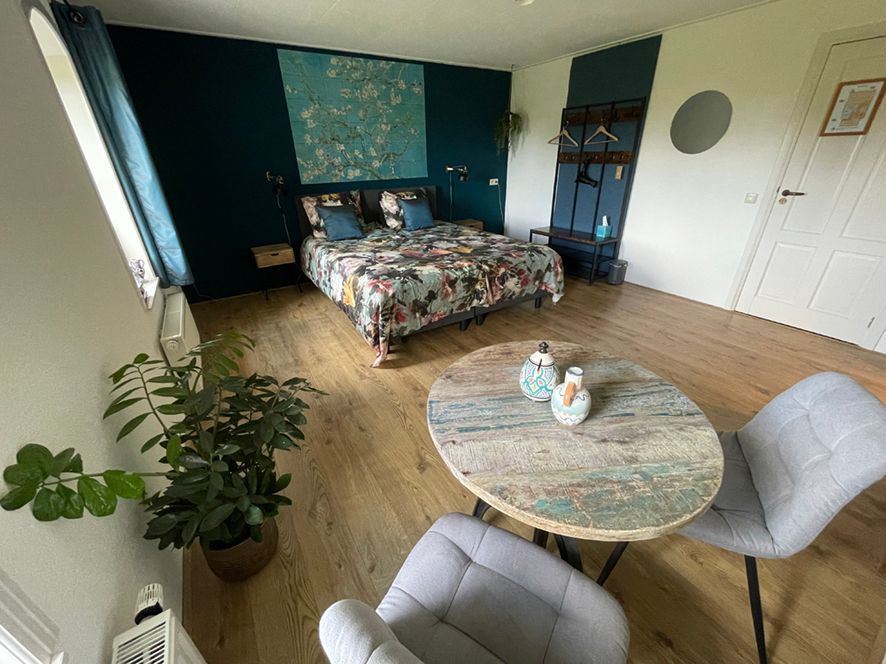 Slaapkamer met bed, ronde tafel, stoelen en een accentmuur geschilderd in turquoise en blauwgroen.