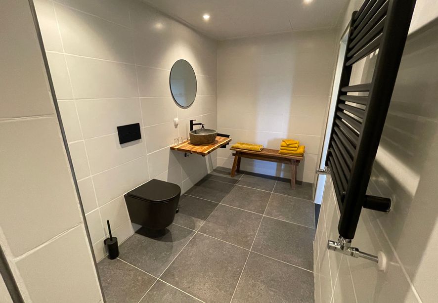 Moderne badkamer met grijze tegels, zwart toilet, wastafel en radiator.