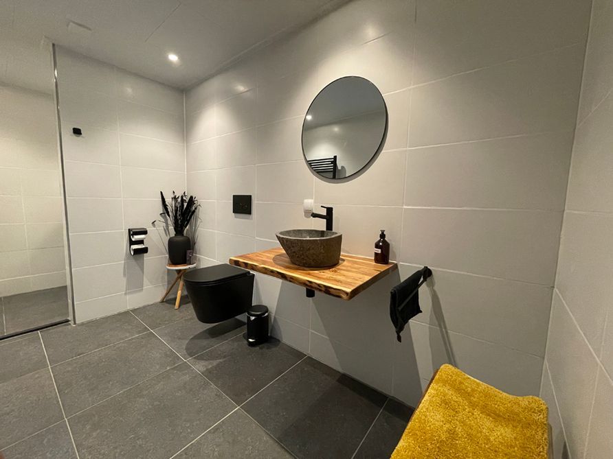 Moderne badkamer met zwevende wastafel, ronde spiegel, zwart toilet en gele handdoek.