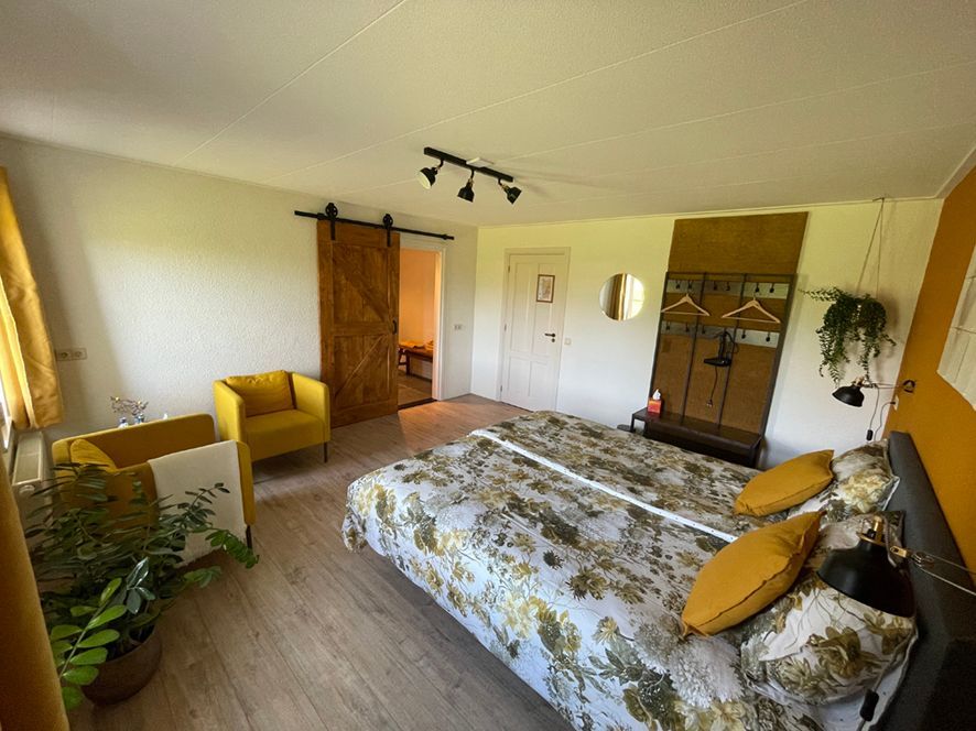 Slaapkamer met houten vloer, gele accenten, kingsize bed, schuifdeur en fauteuil.