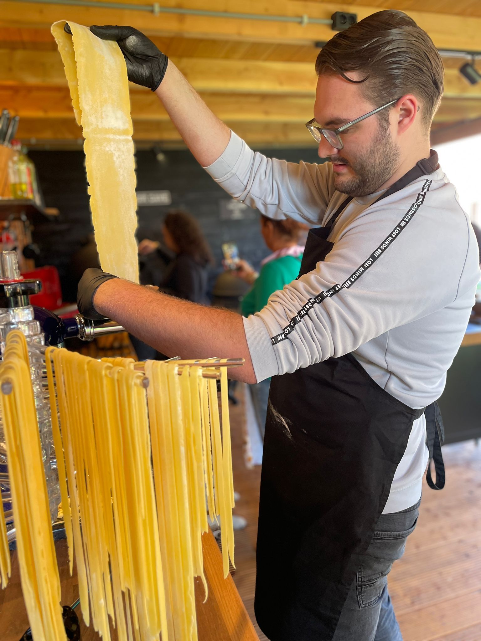 Een chef-kok maakt pasta met een pastamachine; hij houdt een groot vel verse pasta omhoog.