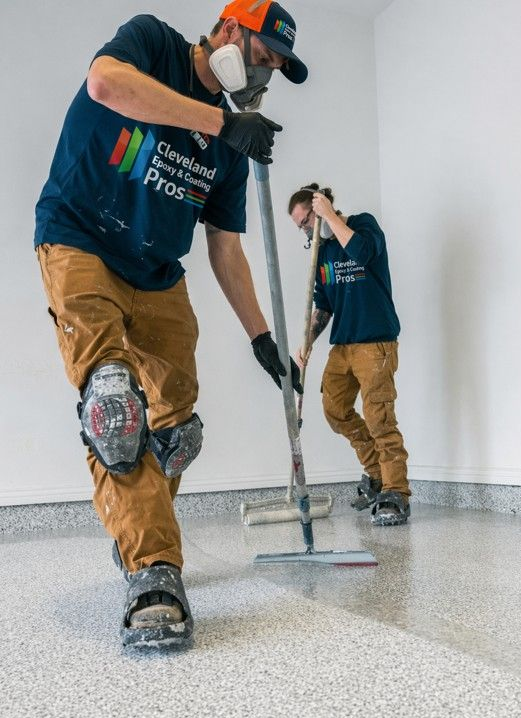 Two workers in blue shirts and tan pants cleaning a speckled floor with a power scrubber and mop