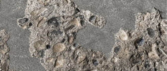 Close-up of cracked, chipped, and pitted concrete with exposed aggregate, showing the kind of worn surface that can make a garage or concrete floor look rough and neglected.