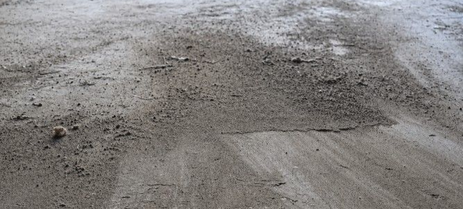Dusty bare concrete floor showing the kind of surface that flake floor coating helps improve. Dusty bare concrete floor in a garage showing loose surface dust and an unfinished appearance that can make the space harder to keep clean and maintain.