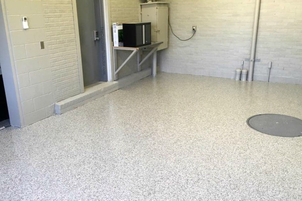 A person stands outside a garage next to a service van, looking over a newly coated, speckled grey concrete floor.