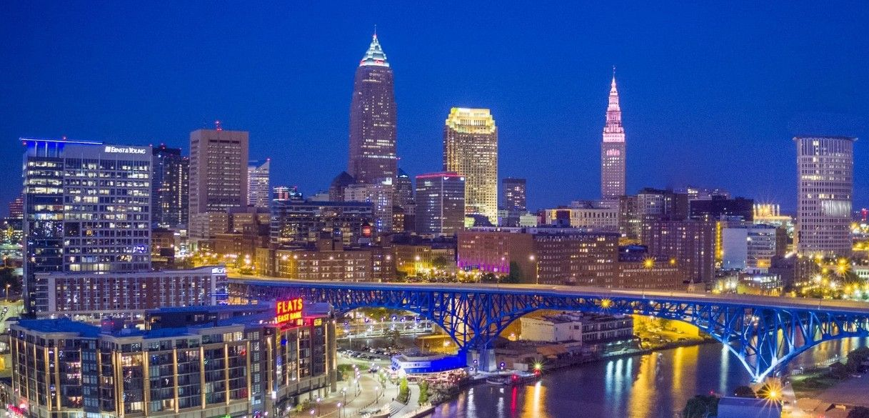 Cleveland skyline at dusk with illuminated buildings and a lit bridge over the river. Cleveland Epoxy & Coating Pros specializes in solving this area's problems for concrete flake floor coatings.