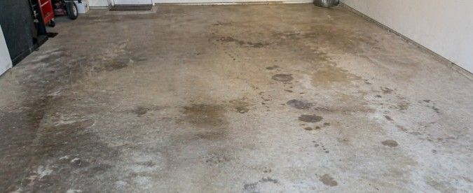 Stained and discolored concrete garage floor with blotchy marks, oil spots, and uneven coloration showing how untreated concrete can look worn over time.