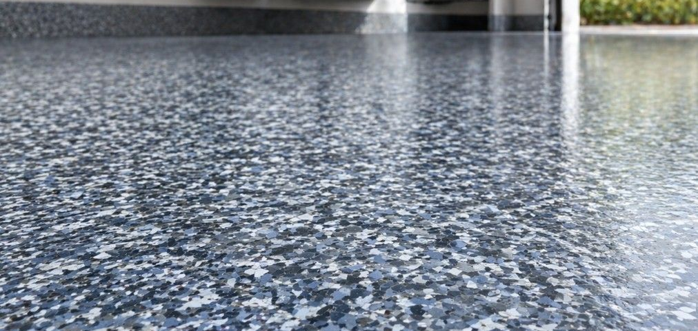 Close-up of a professional flake floor coating system in a clean garage, showing the textured multi-tone flake broadcast, smooth finished surface, and refined appearance that sets flake flooring apart from bare concrete and standard floor paint.