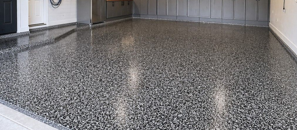 Wide view of a professionally coated garage floor with a decorative black, gray, and white flake epoxy finish, showing how flake floor coating works well in practical spaces that need durability, visual appeal, and easier maintenance.